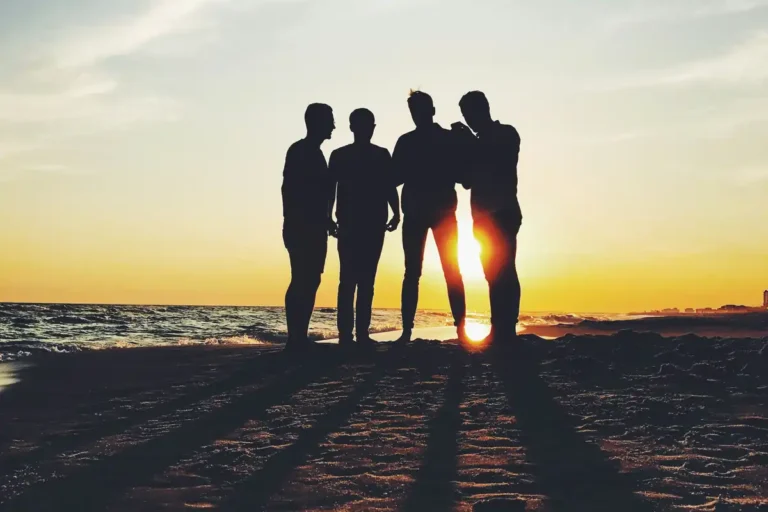 Four friends silhouetted against a sunset on the beach